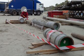 Worker inspecting pipes near safety barrier.