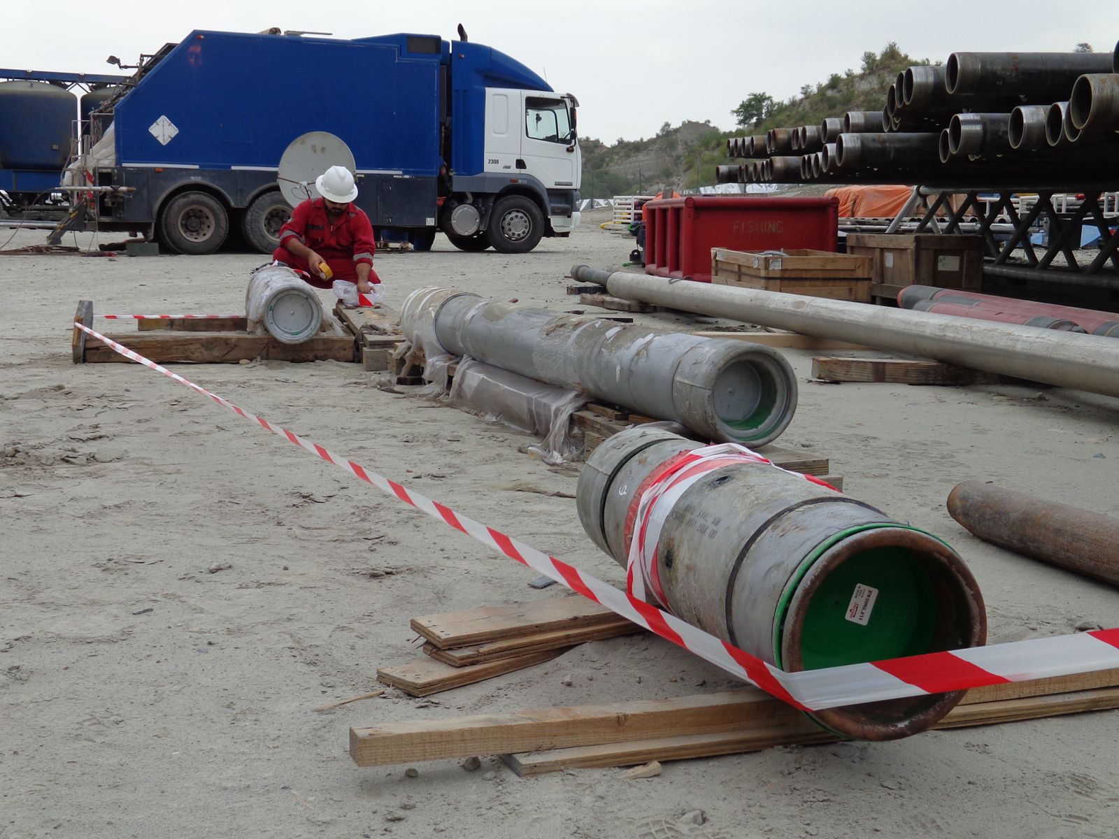 Worker inspecting pipes near safety barrier.